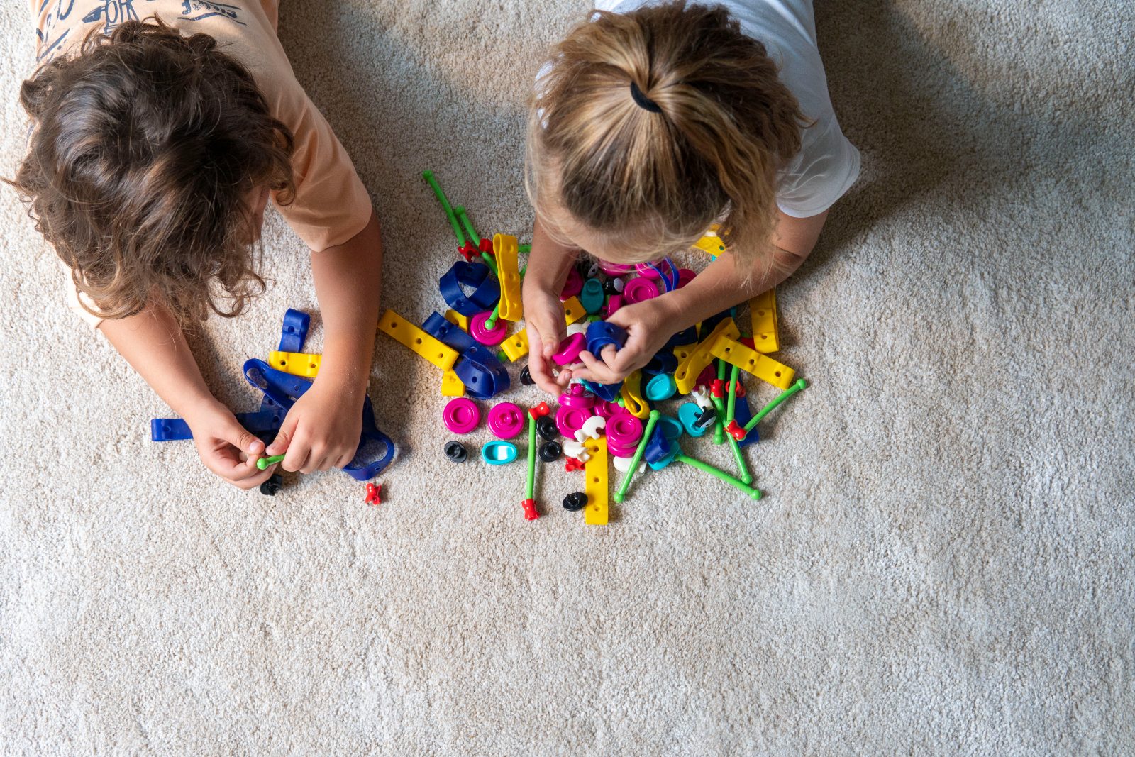 Two children building with colorful Toyi pieces on a rug
