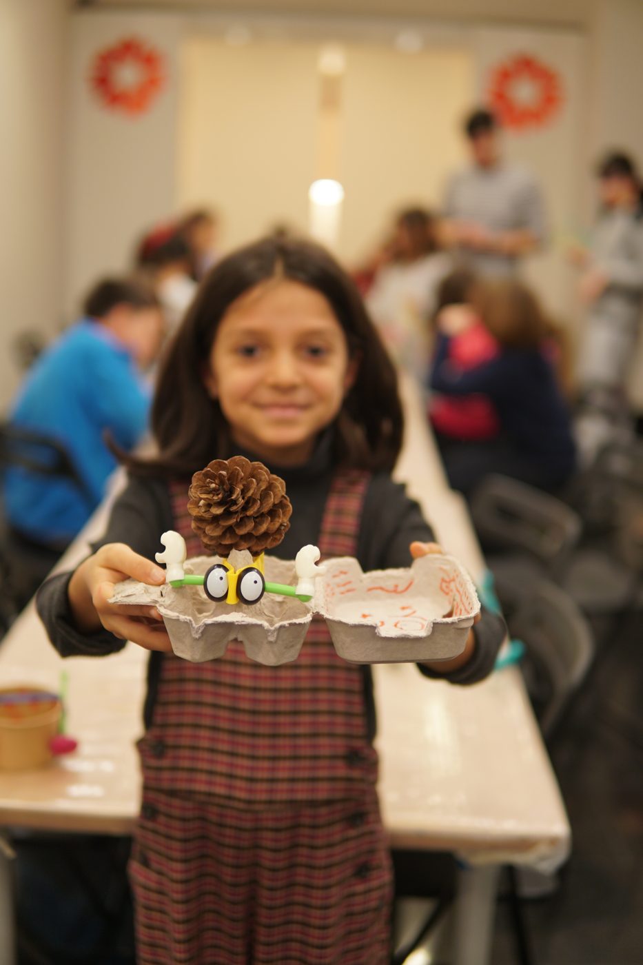 A smiling girl holding a creature made from an egg box and a pine cone